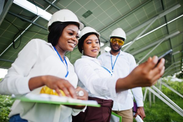 African american technician checks the maintenance of the solar panels. Group of three black engineers meeting at solar station. Make selfie by phone.